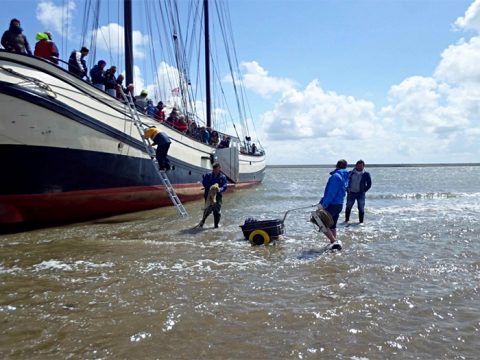 Cursisten klimmen van de boot het wad op