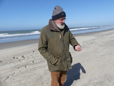 Bioloog Arthur Oosterbaan op een zonnig strand, dikke kleren aan en muts op, want het is wel fris.