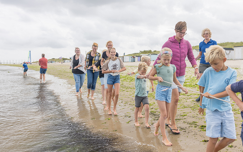 Groep kinderen en volwassenen trekken touw van sleepnet over het strand